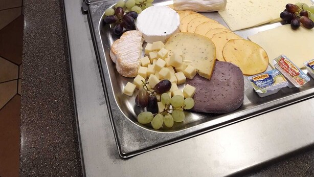 Een buffet met diverse gerechten, waaronder vleeswaren, kazen en fruit.