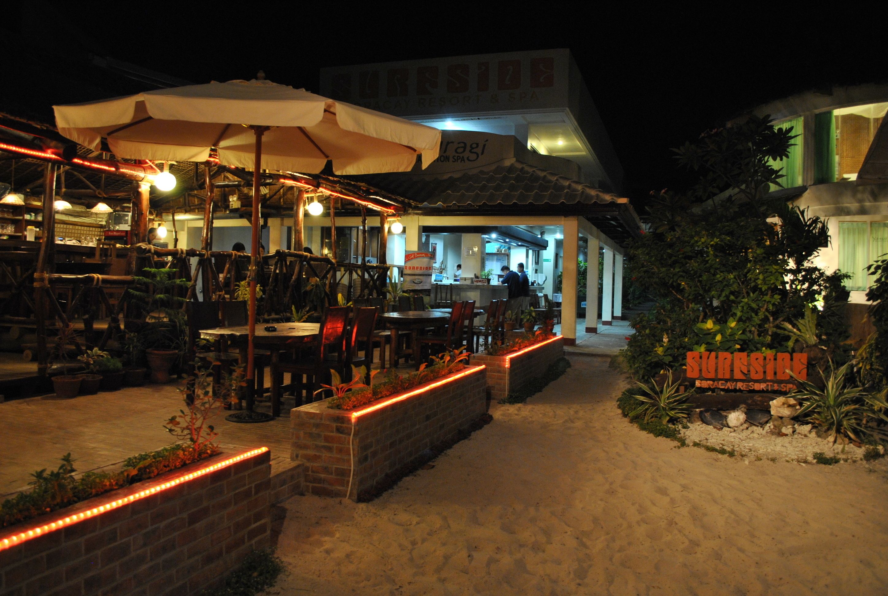 A restaurant with outdoor seating, umbrellas, and a sign for Sunrise Resort & Spa.