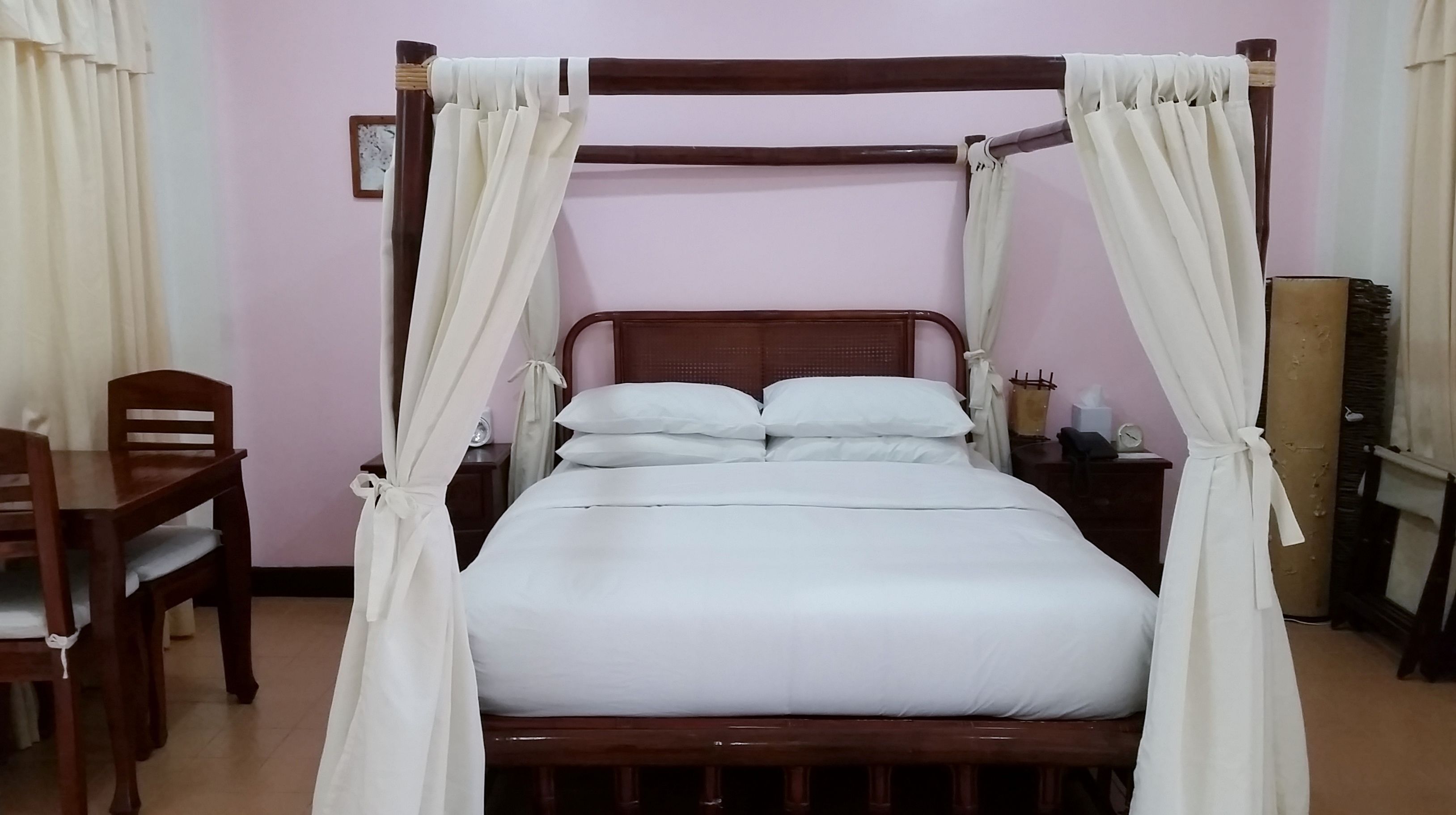 Una cama con dosel con ropa blanca, cabecera de madera y cortinas.