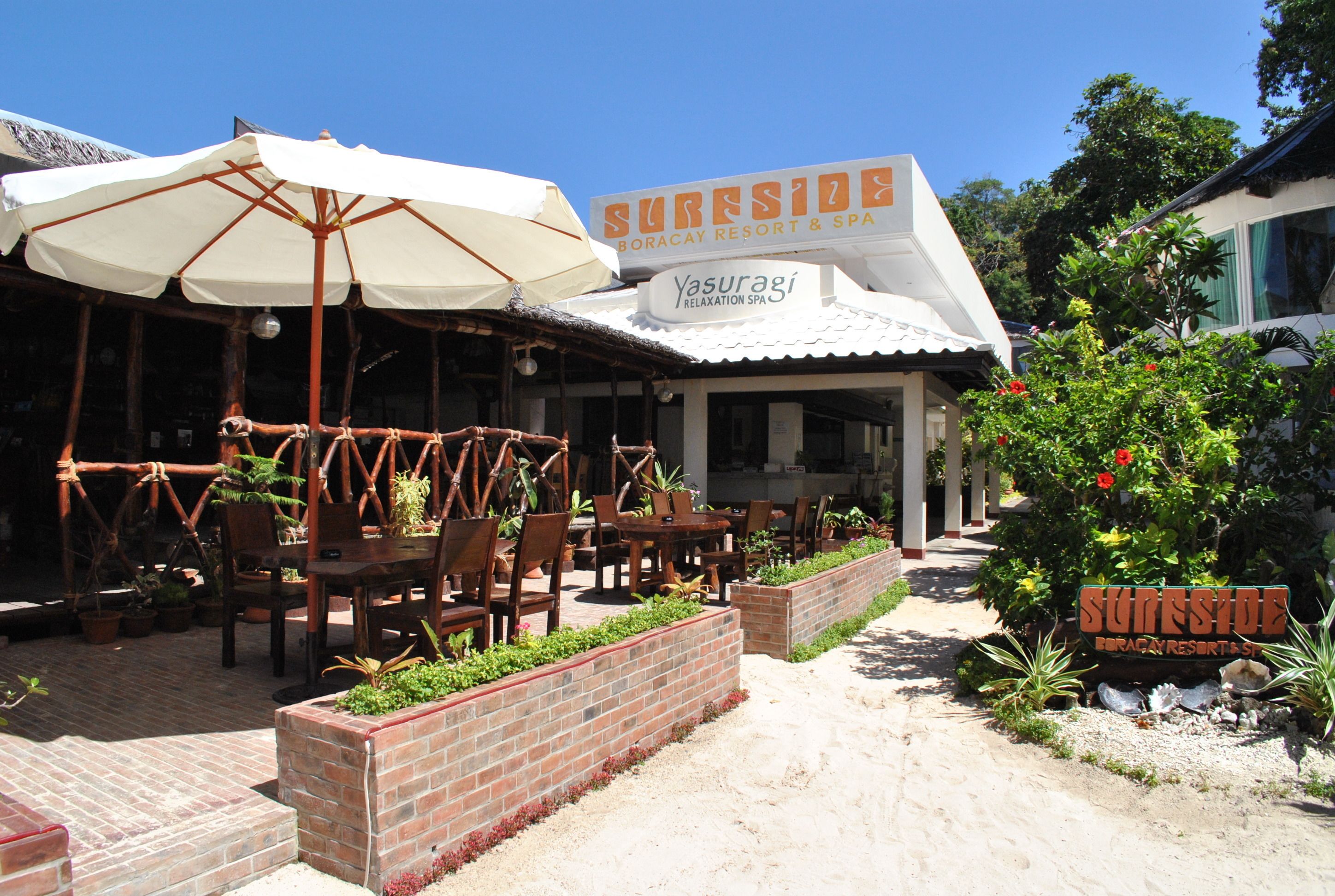 Et resort med udendørs siddepladser, et skilt med 'Sureside Boracay Resort & Spa' og en sti til indgangen.