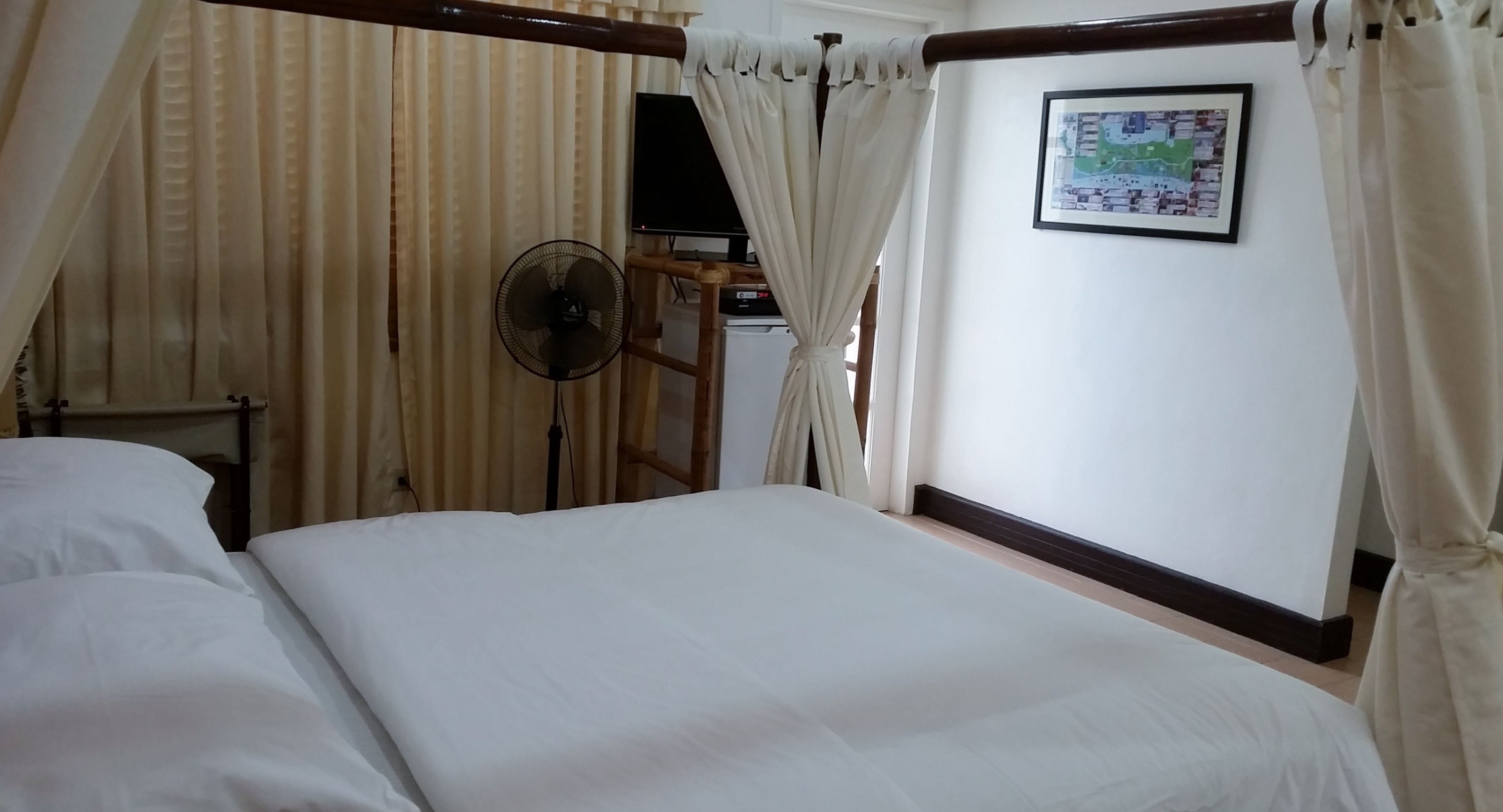 Un dormitorio con una cama, un ventilador, cortinas, un televisor y un mapa enmarcado en la pared.