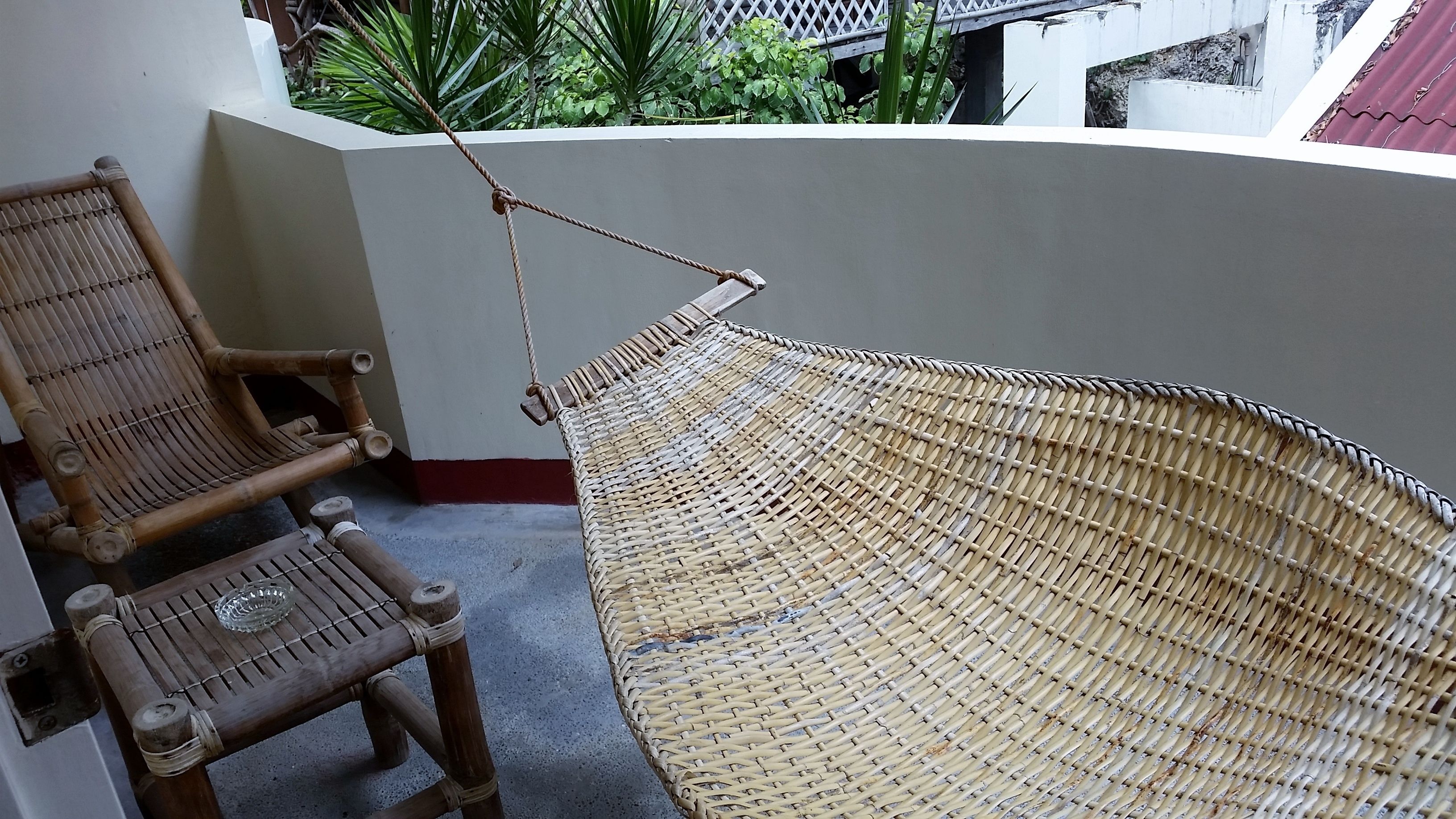A hammock tied to a balcony railing, with two wooden chairs nearby.