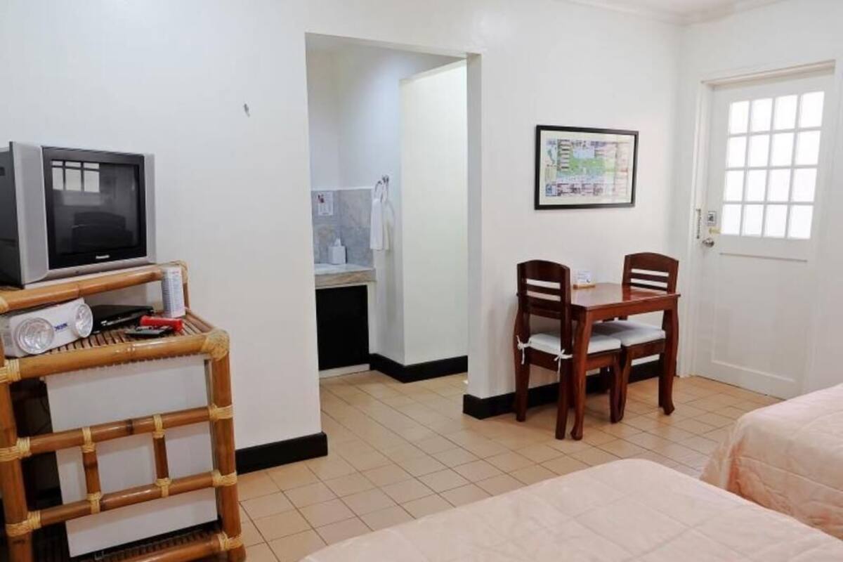 A hotel room with a bed, a desk with a chair, a television, and a bathroom visible through an open door.