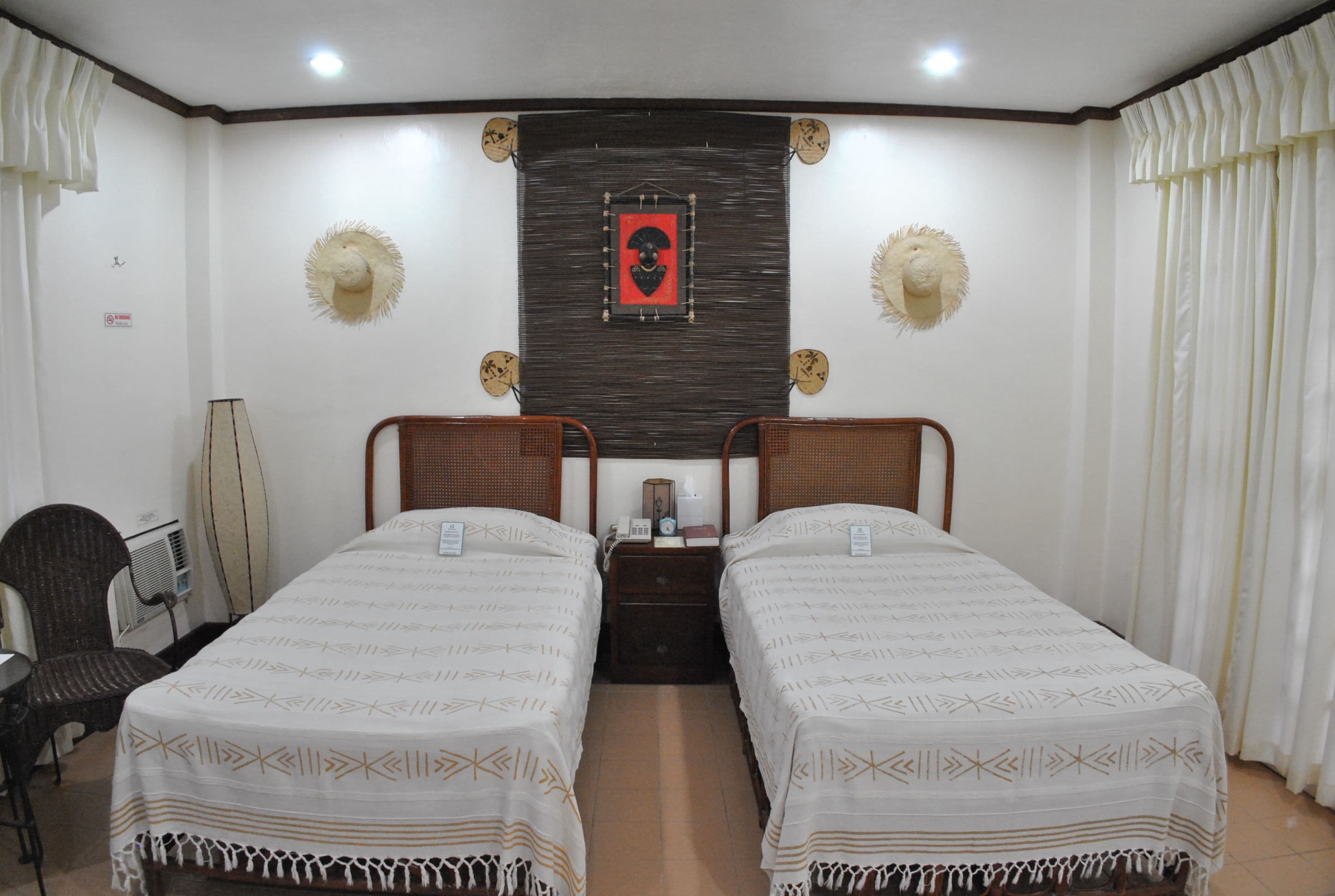 A room with two single beds, a chair, a desk, and a surfboard.
