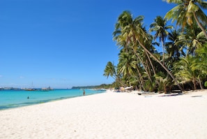 A beach with white sand, palm trees, and boats in the water. - Surfside Boracay Resort (Boracay Island)