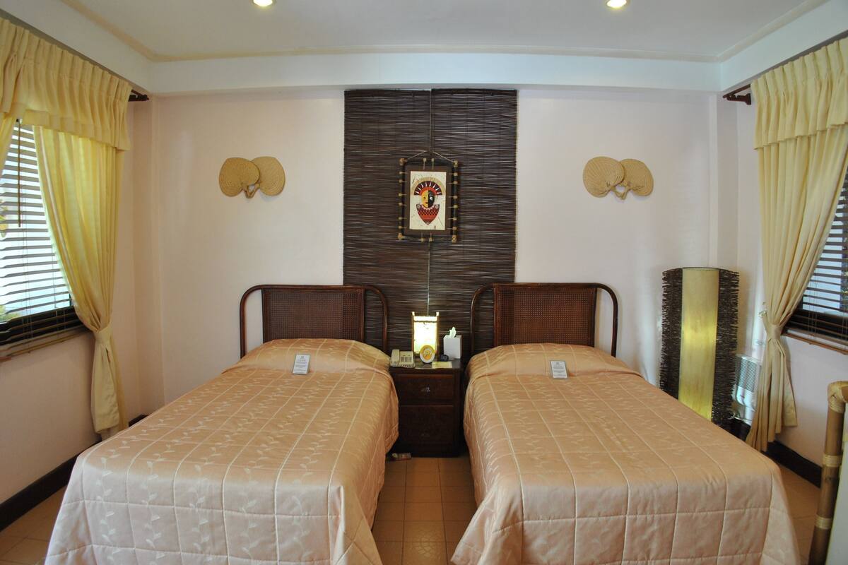 A hotel room with two single beds, a bedside table with a lamp, and a wall-mounted decorative piece.