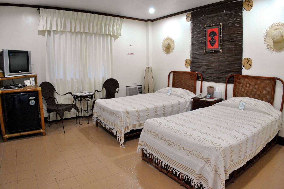 A hotel room with two single beds, a desk with a chair, a television, and a minibar.