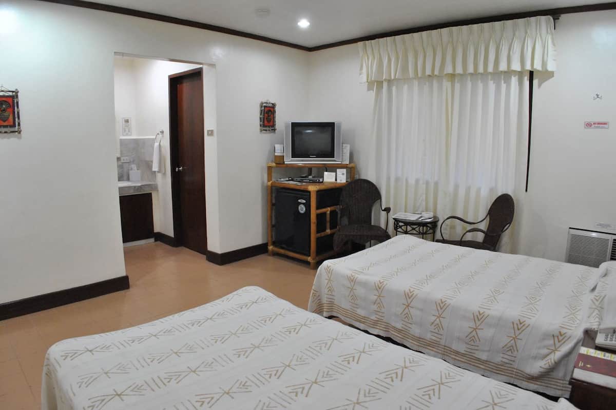 A hotel room with two beds, a desk with a computer, a chair, a small table, and a window with curtains.