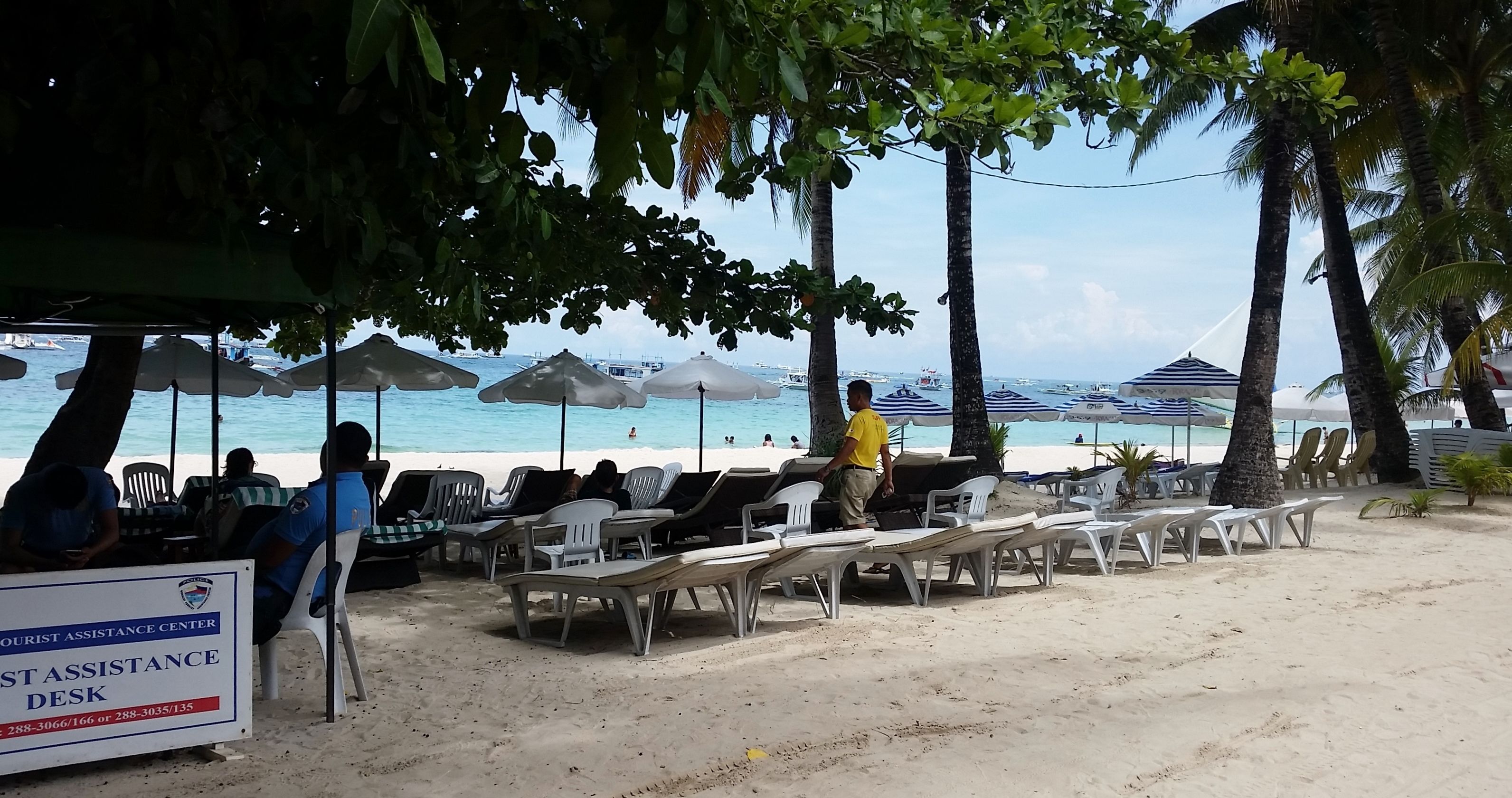 Ein Touristeninformationszentrum direkt am Strand, mit Schildern, weißen Liegestühlen und Sonnenschirmen.