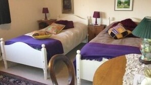 Un dormitorio con dos camas, cada una con una colcha y almohadas moradas, una mesita de noche con una lámpara y una silla.