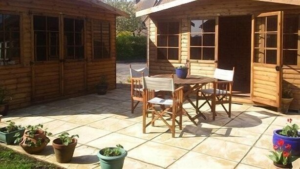 Una cabaña de madera con un patio amoblado, que incluye una mesa y sillas, rodeada de macetas con plantas.
