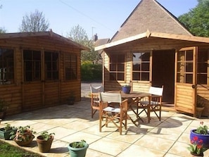 A wooden cabin with a patio area featuring a table and chairs, surrounded by potted plants. - Avebury Life B&B (Marlborough)