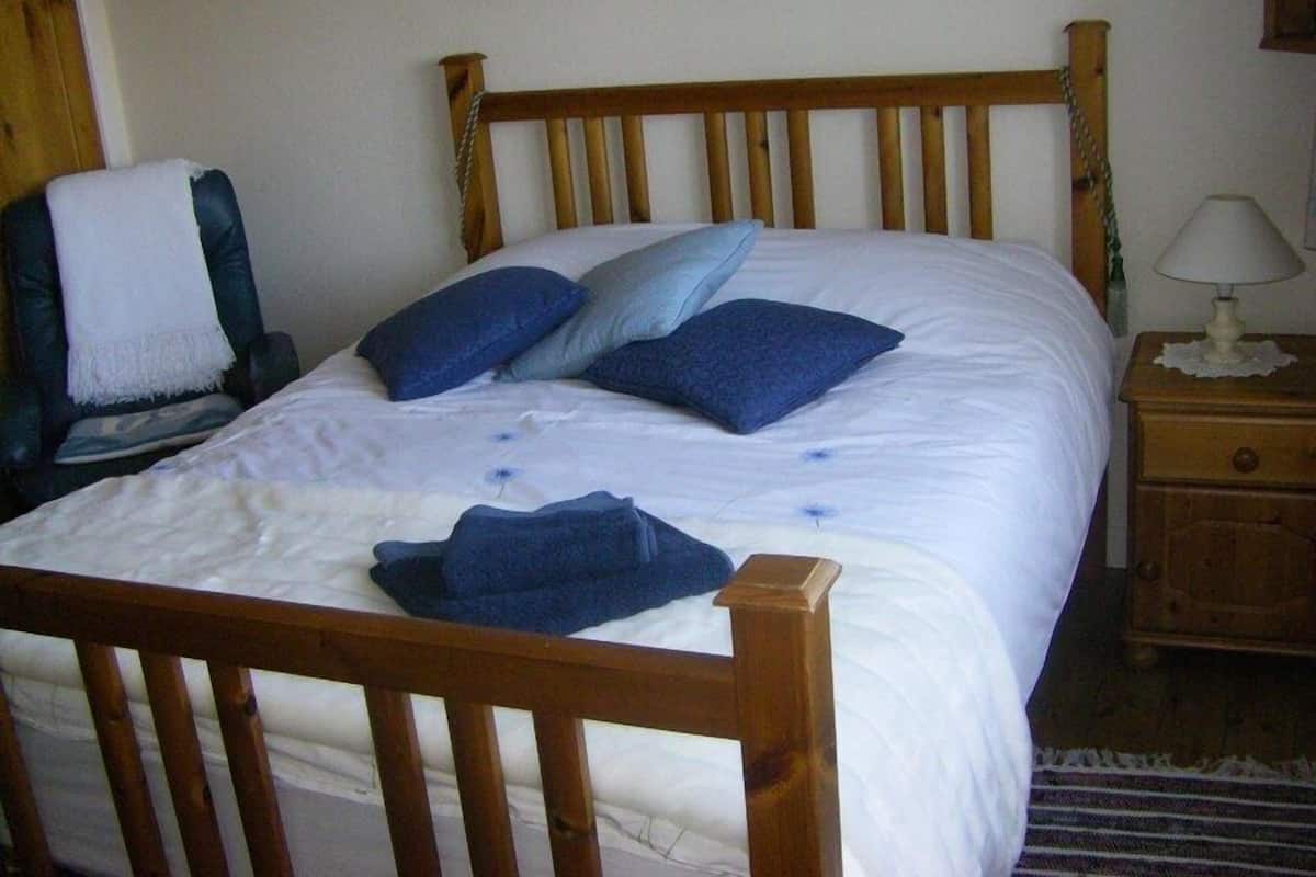 A neatly made bed with a wooden headboard, a chair with a white towel, and a nightstand with a lamp.