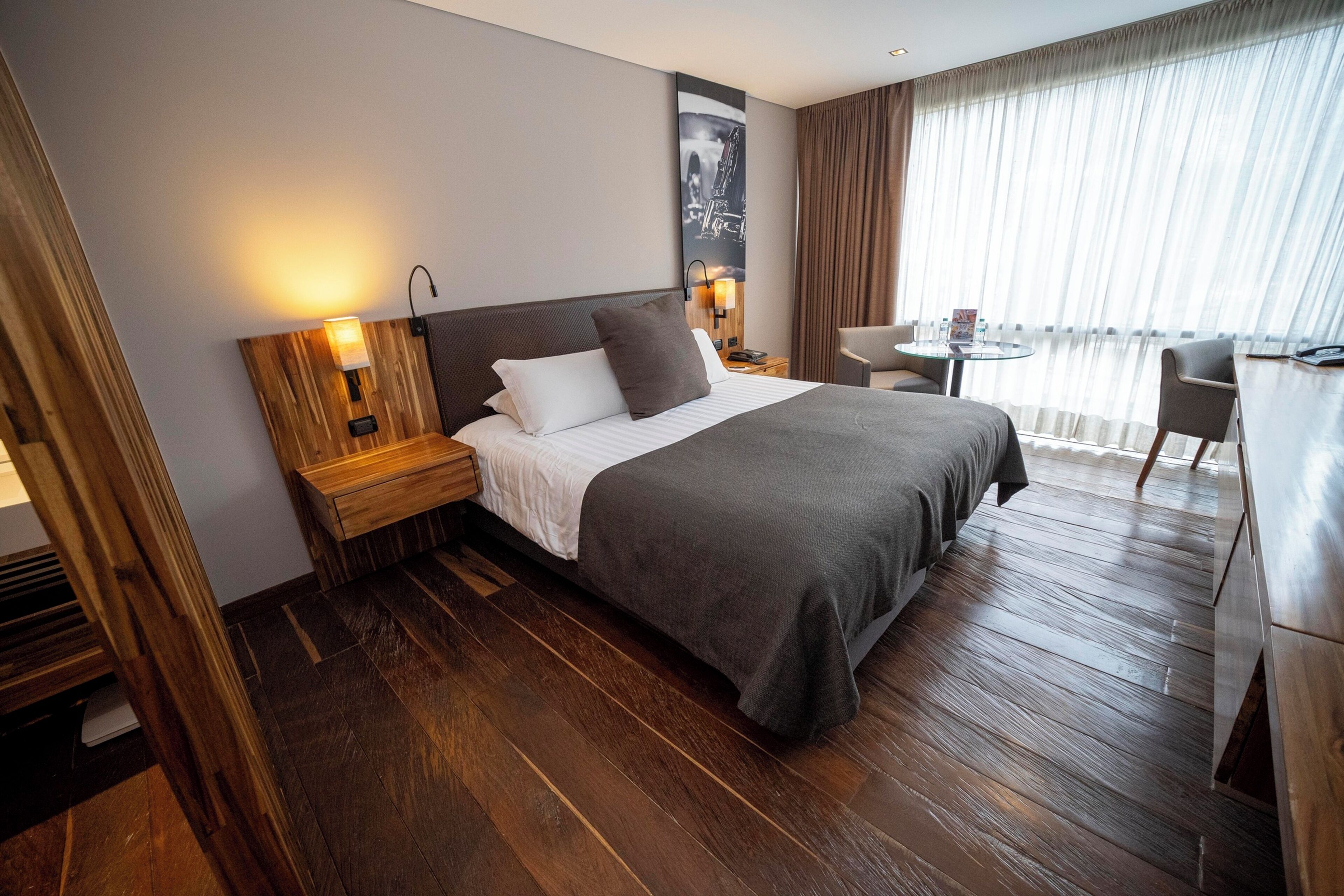 A hotel room with a large bed, a wooden headboard, a nightstand, a desk, and a chair.