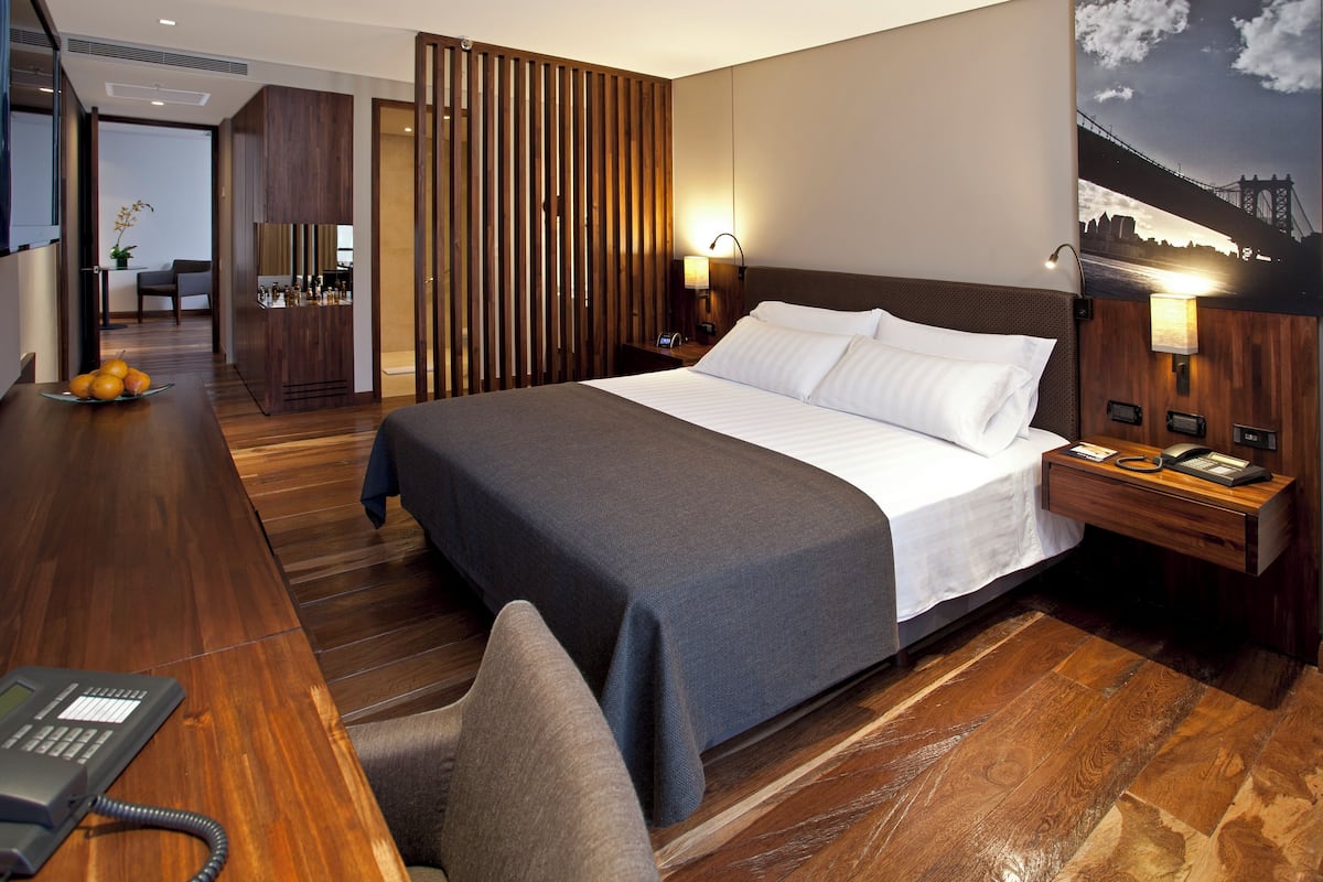 Une chambre d’hôtel avec un grand lit, un plancher en bois, un bureau avec un téléphone et une table de chevet avec une lampe.