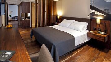 Habitación de hotel con una cama grande, suelo de madera, un escritorio con teléfono y una mesita de noche con lámpara.