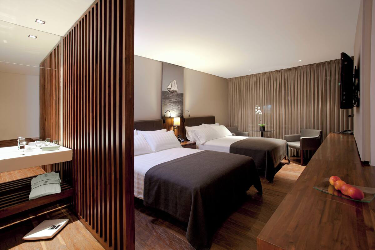 Une chambre d’hôtel avec deux lits, un bureau en bois, une télévision et une salle de bain.