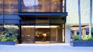Ein moderner Hotel Eingang mit Glasfassade, ein Mann liest ein Buch und Zimmerpflanzen.
