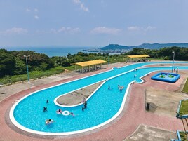Uma grande piscina ao ar livre com design sinuoso, rodeada por um calçadão de tijolos e uma área coberta para sentar.
