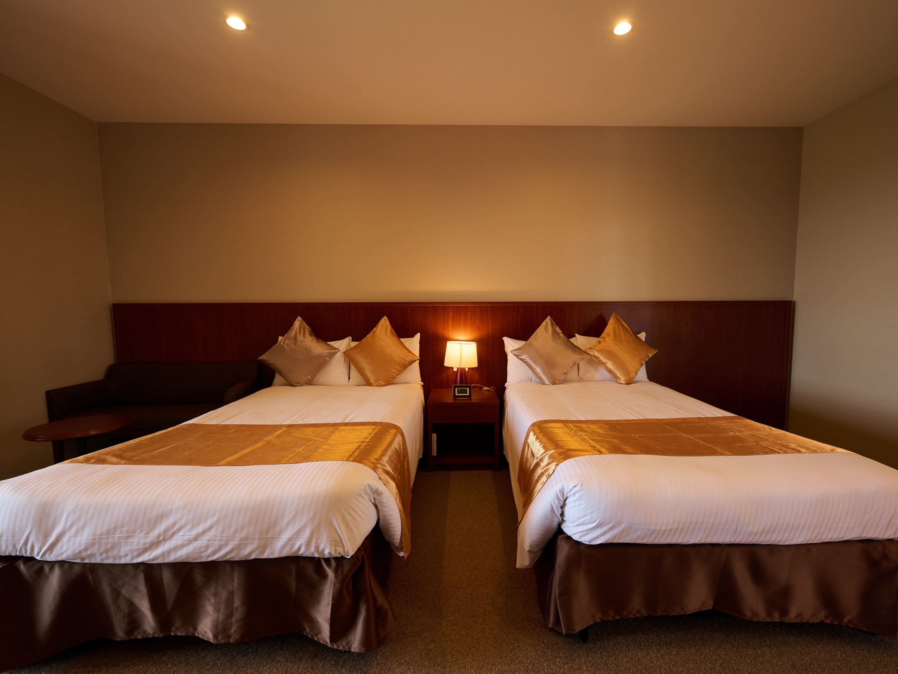 A hotel room with two beds, a nightstand with a lamp, and a wall-mounted light fixture.