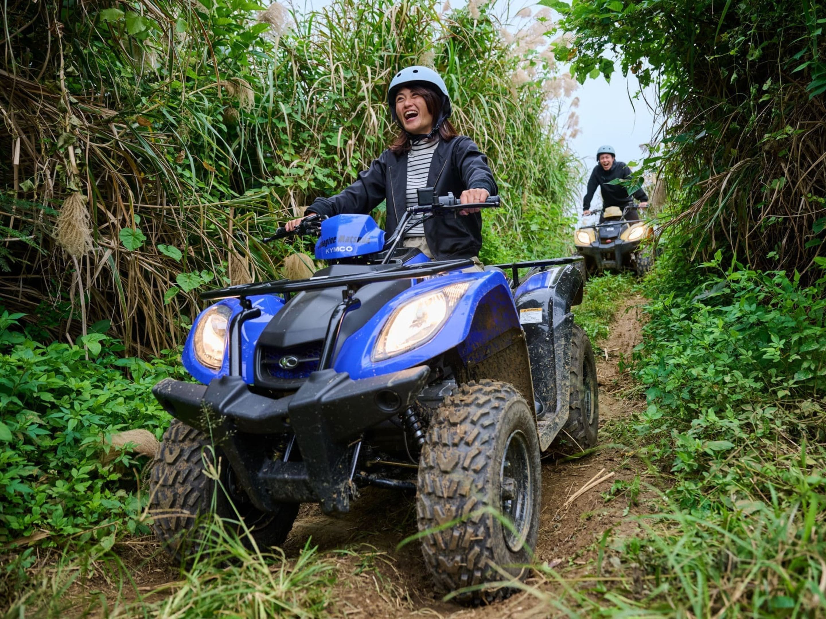A person riding a blue ATV on a dirt path surrounded by dense vegetation.