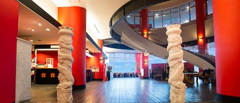 A modern hotel lobby with a curved staircase, red walls, and a reception area.
