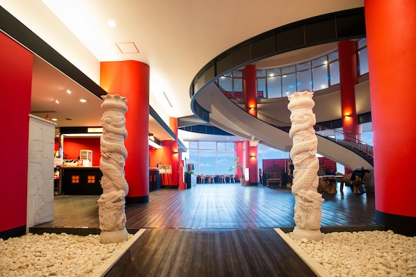 Un moderno vestíbulo de hotel con una escalera curva, paredes rojas y una zona de recepción.