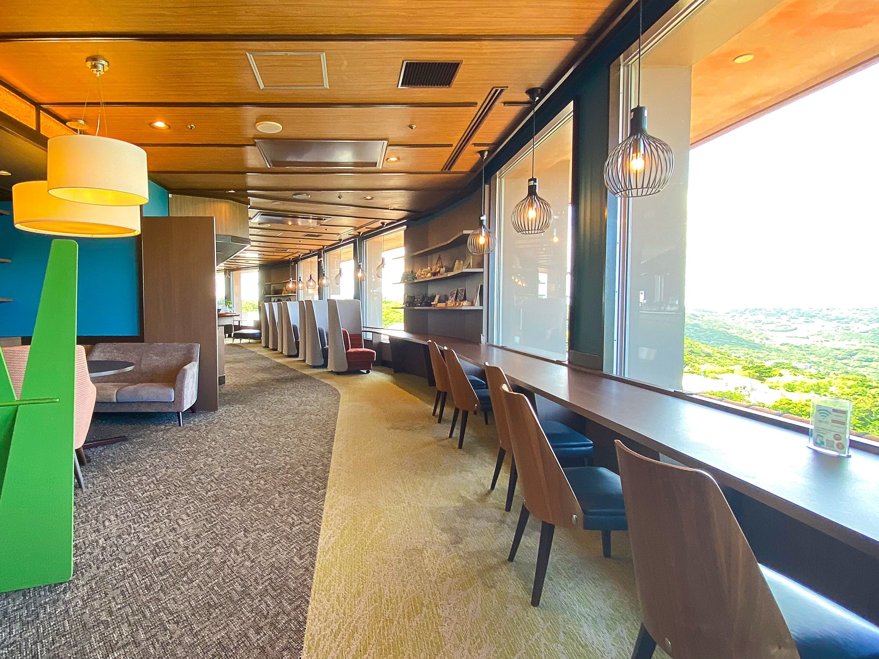 A modern dining area with a long table and chairs, large windows offering a view of the landscape, and a variety of pendant lights.