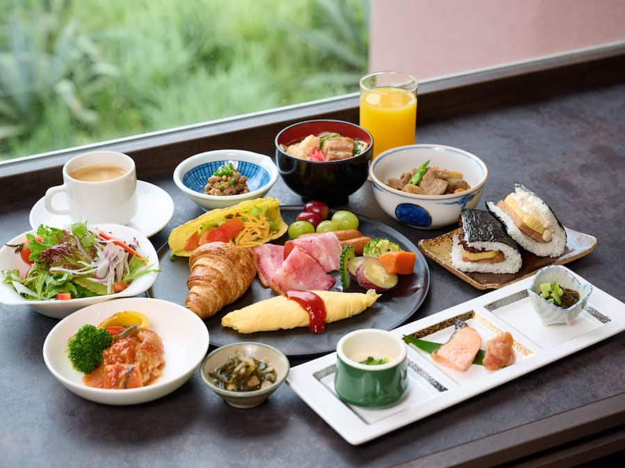 Diversos itens de café da manhã, incluindo croissants, omeletes e sushi, em uma bandeja.