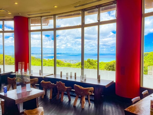 Un restaurante moderno con amplios ventanales que ofrece una vista panorámica del mar y la vegetación.