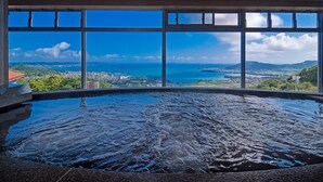 A hot tub with a panoramic view of a coastal city through large windows. - Wellness Resort OKINAWA The Yuinchi Hotel Nanjo (Nanjo)