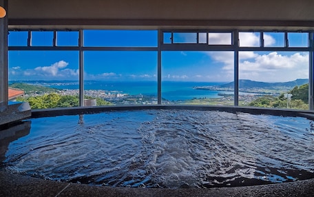 A hot tub with a panoramic view of a coastal city through large windows.
