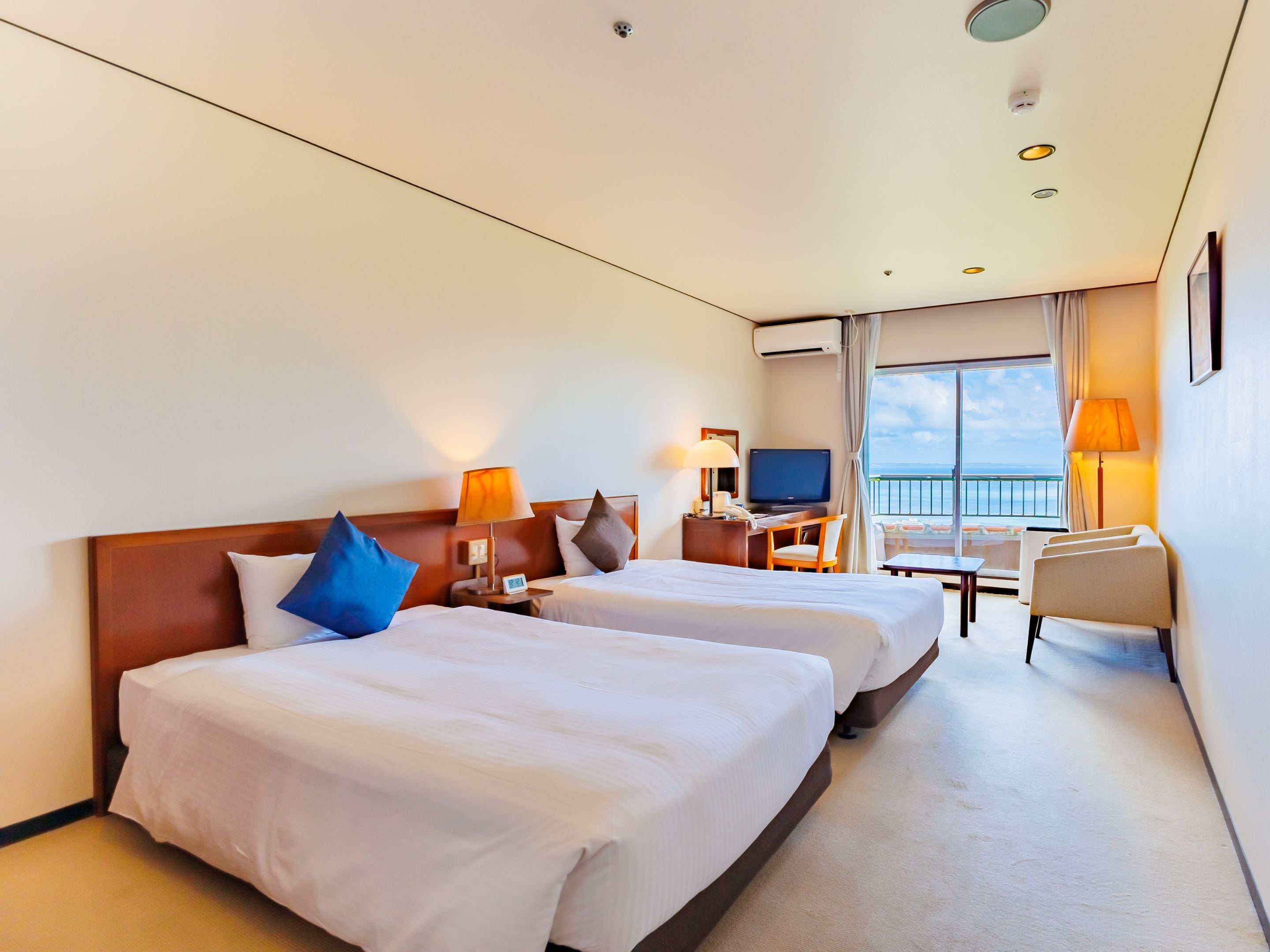 Habitación de hotel con dos camas, un escritorio, un televisor y vistas al mar.