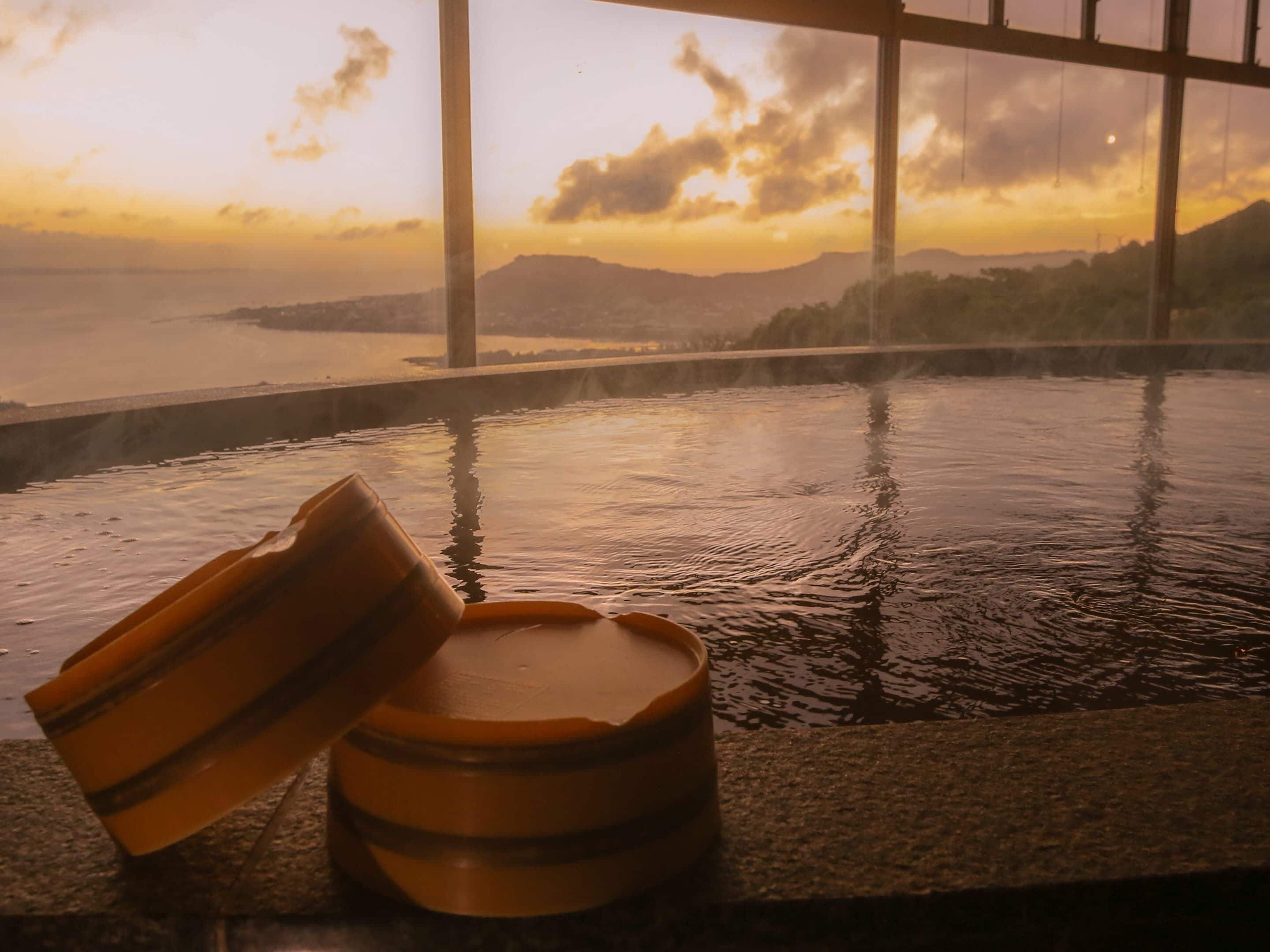 A hot tub with a view of a sunset over a body of water and mountains.