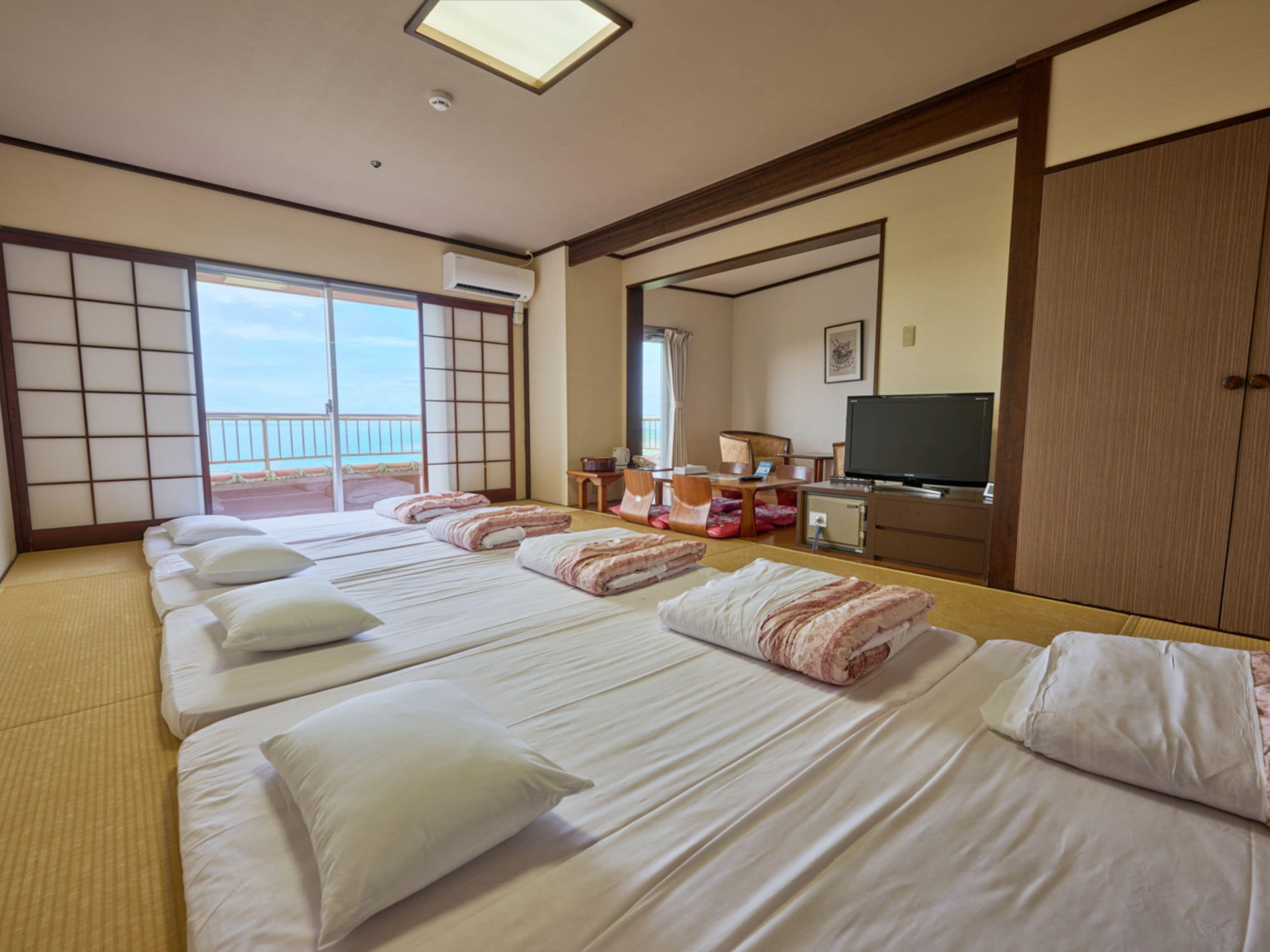 A hotel room with tatami flooring, a sliding door to a balcony, a television, and a desk with a chair.