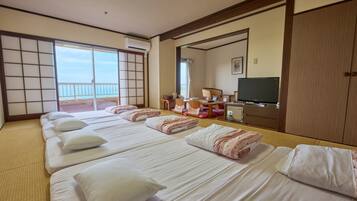 A hotel room with tatami flooring, a sliding door to a balcony, a television, and a desk with a chair.