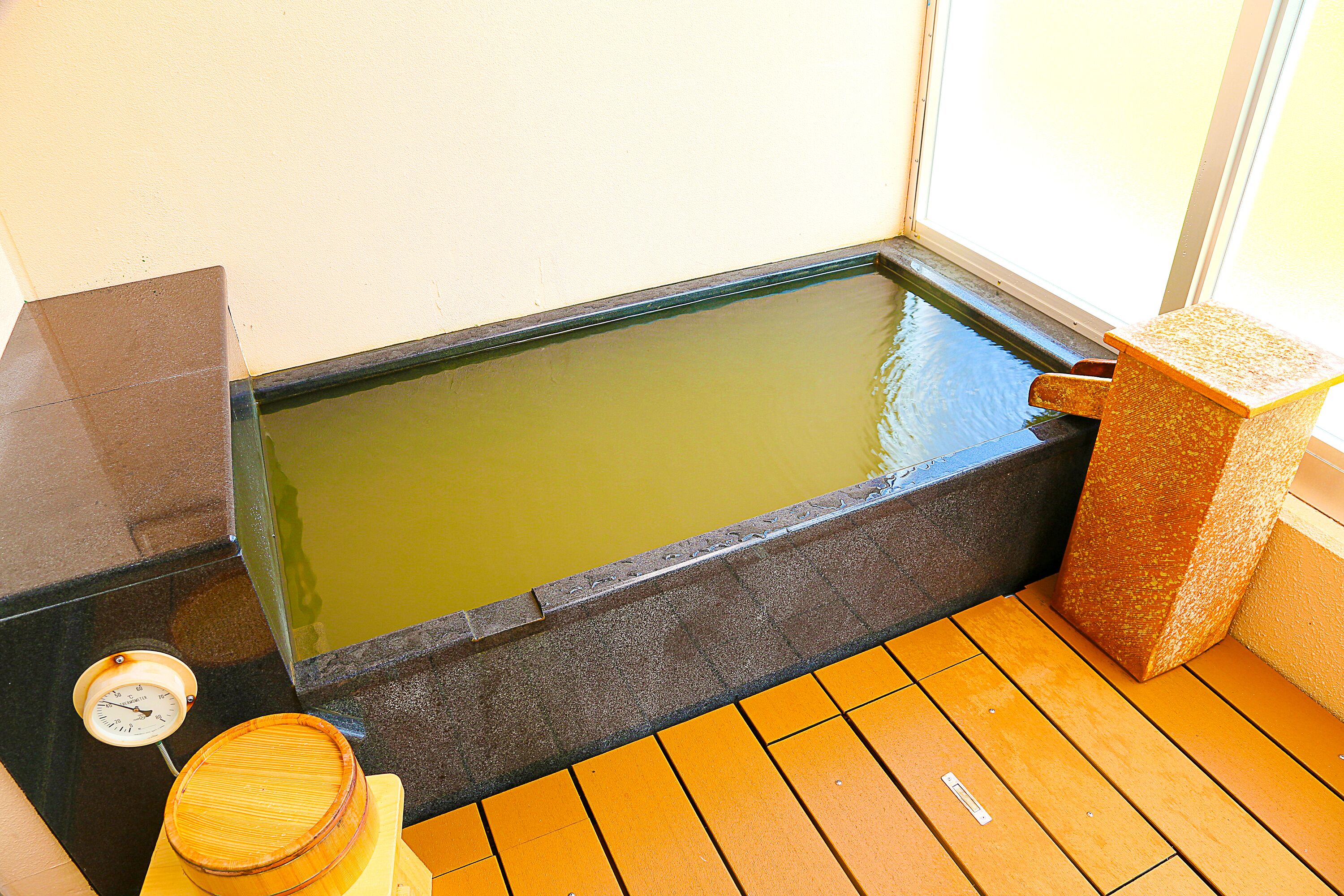 A hot spring bath with a wooden floor, a stone basin, and a wooden stool.