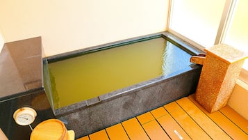A hot spring bath with a wooden floor, a stone basin, and a wooden stool.