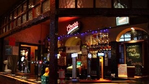 A bar with a neon sign, a chalkboard with writing, and a variety of bottles and glasses.