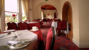 A dining area with tables and chairs, a red carpet, and a view through an archway.
