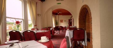 A dining area with tables and chairs, a red carpet, and a view through an archway.