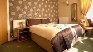 A hotel room with a large bed, a nightstand, a chair, a radiator, and a mirror on the wall.