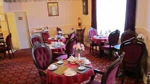 A dining area with round tables covered in red tablecloths, surrounded by velvet chairs. - Sussex Hotel (Blackpool)