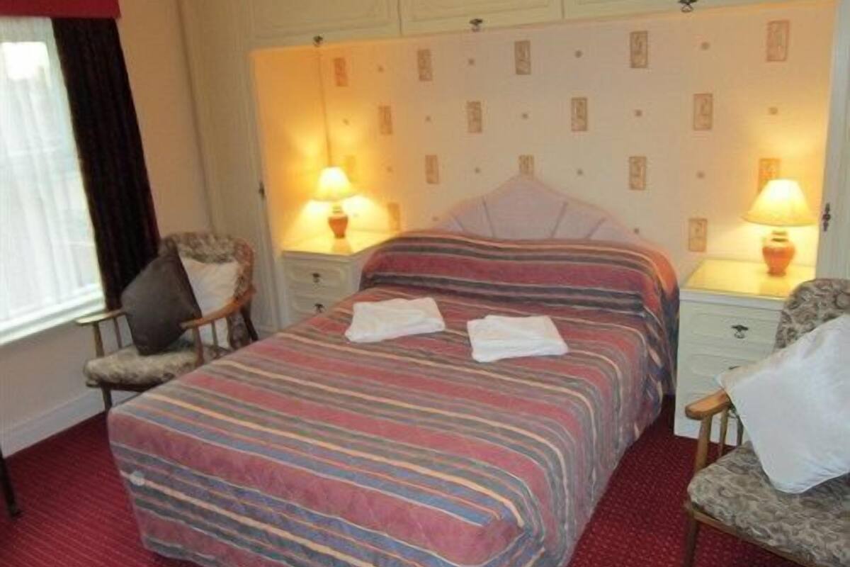 Une chambre d’hôtel avec une couvre-lit à rayures, deux tables de chevet avec des lampes, une chaise et une fenêtre avec des rideaux.