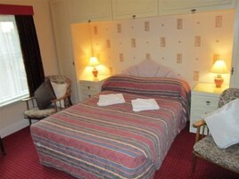 Een hotelkamer met een gestreepte spreideken, twee nachtkastjes met lampen, een stoel en een raam met gordijnen.
