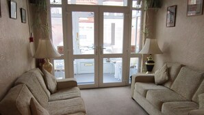 A living room with two beige sofas, a coffee table, and two lamps. There is a glass door leading to an outdoor area with a table and chairs. - Sussex Hotel (Blackpool)