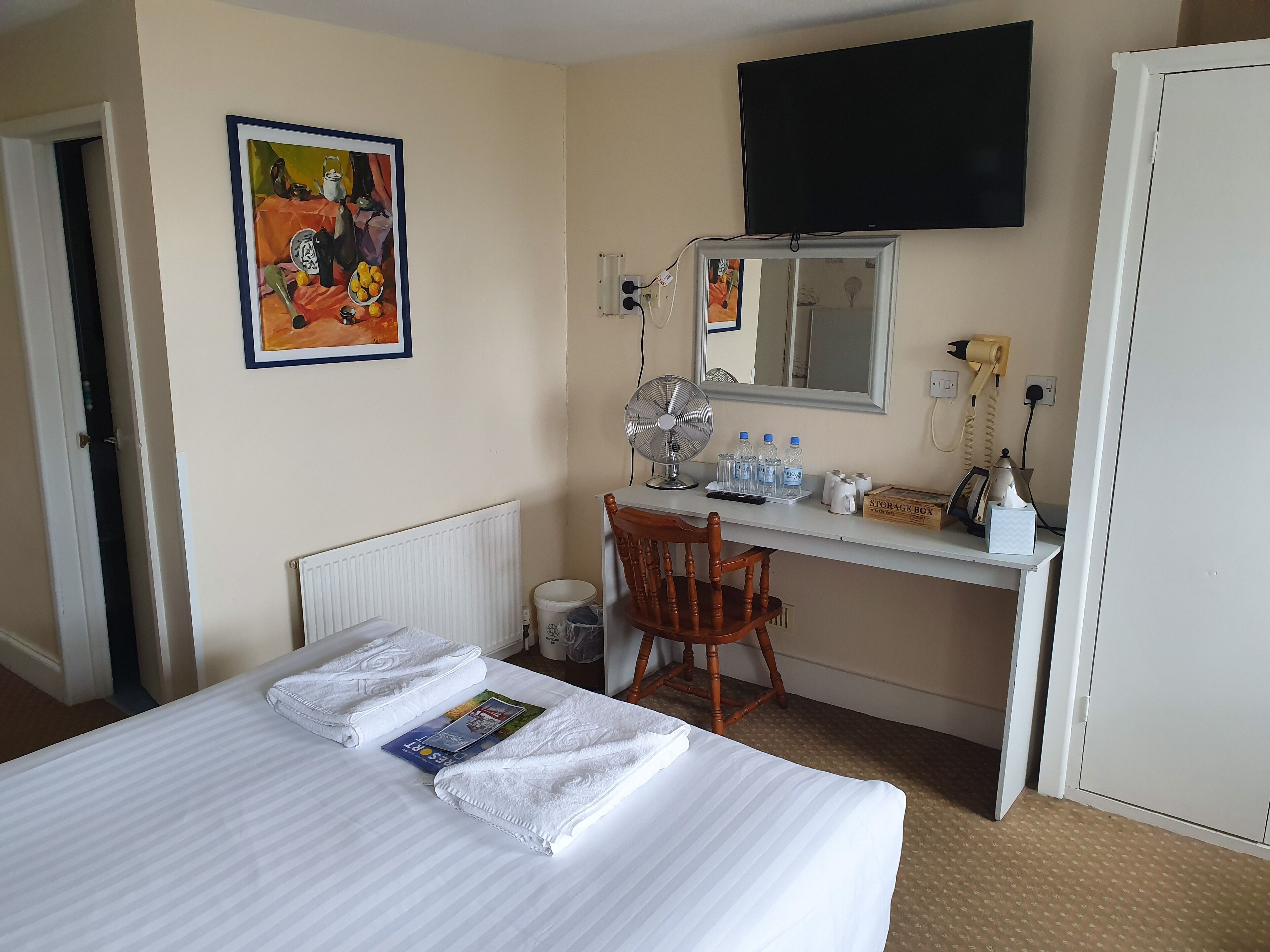A hotel room with a bed, a desk, a chair, a television, and a painting on the wall.