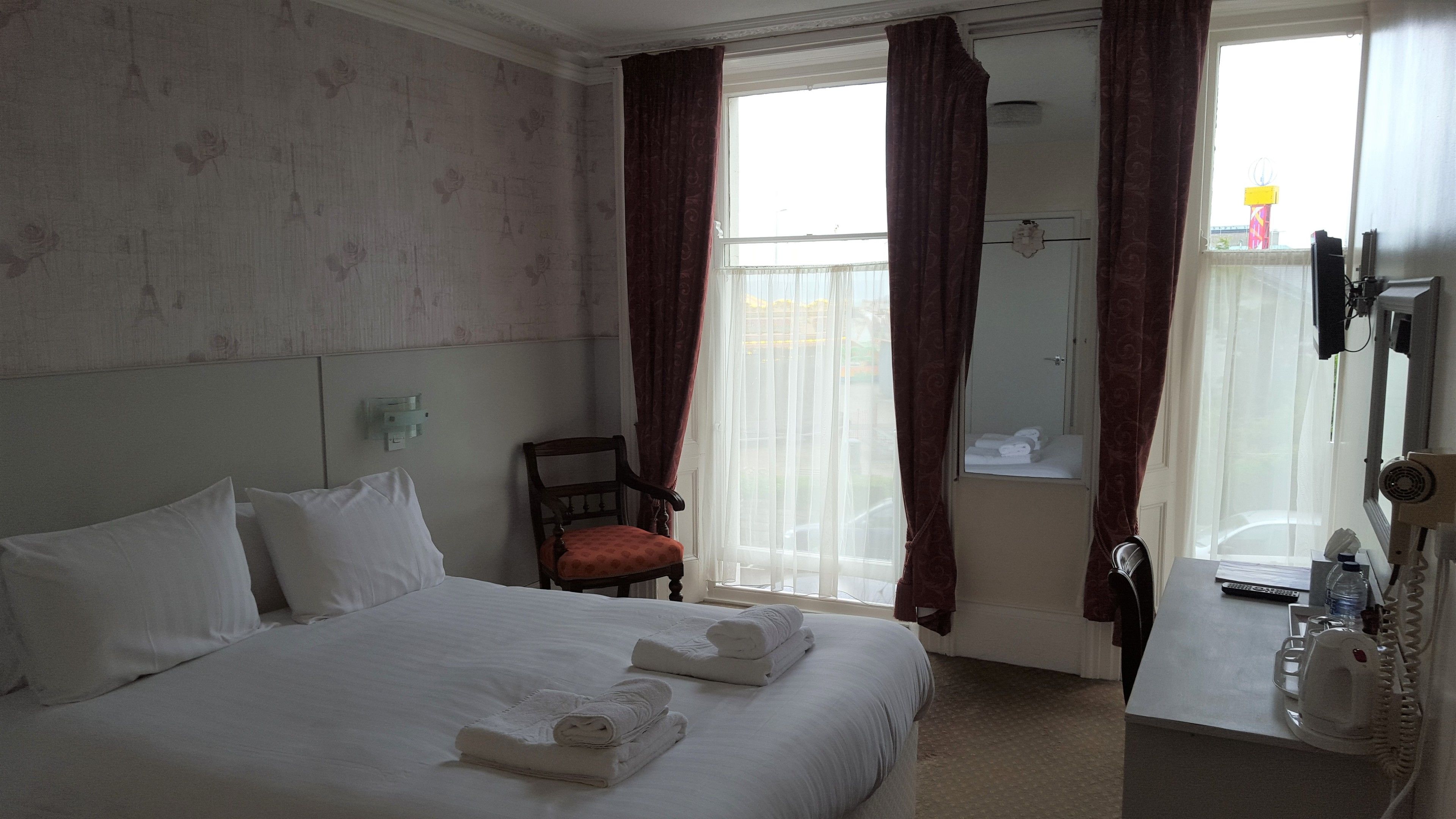 A hotel room with a large bed, a chair, a bathroom with a mirror, and a window with curtains.