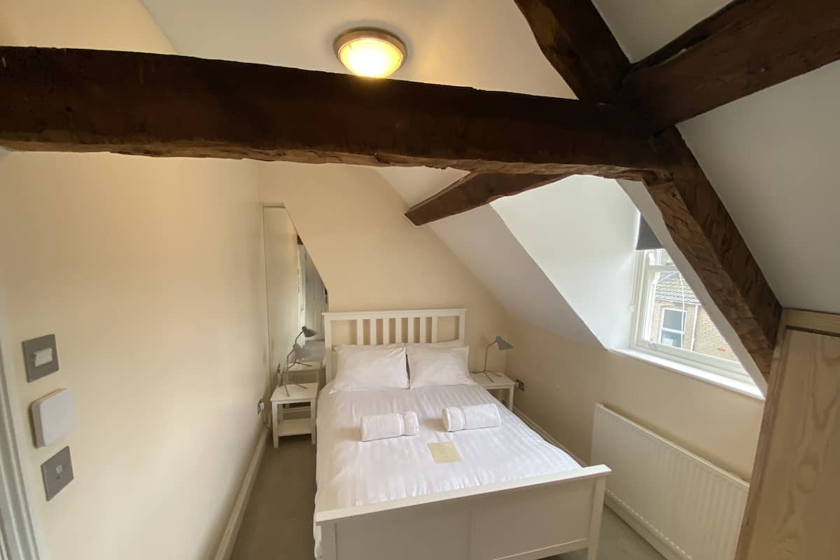 A bedroom with a sloped ceiling, a bed, bedside tables, a lamp, and a window.