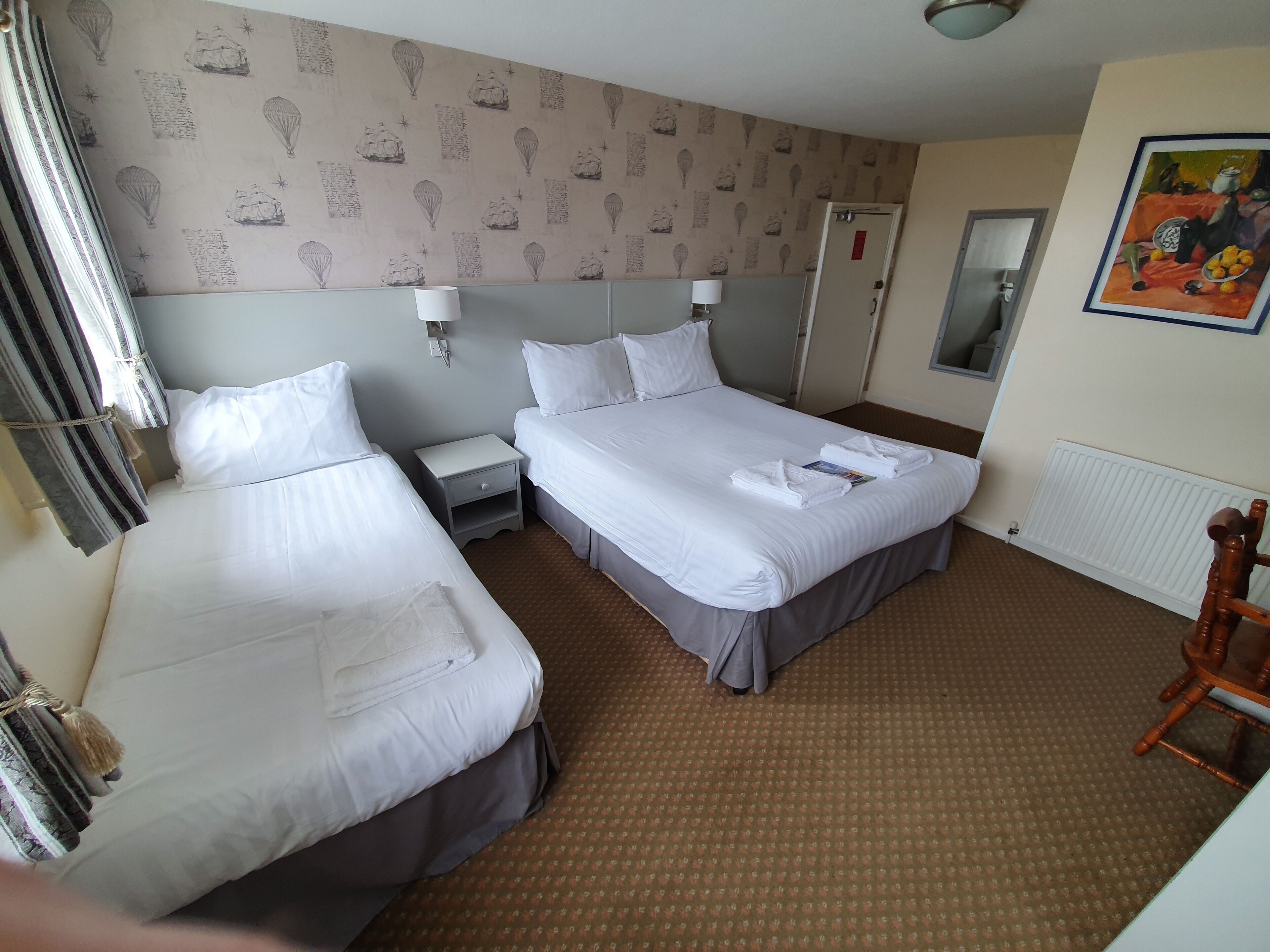 Een hotelkamer met twee bedden, een nachtkastje, een lamp, een radiator en een schilderij aan de muur.